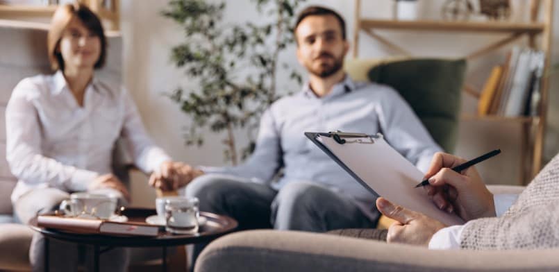 זוג המשתמש בגישור כדי לפתור בעיות משפחתיות בישיבה על כיסא עם לוח כתיבה לפניהם.